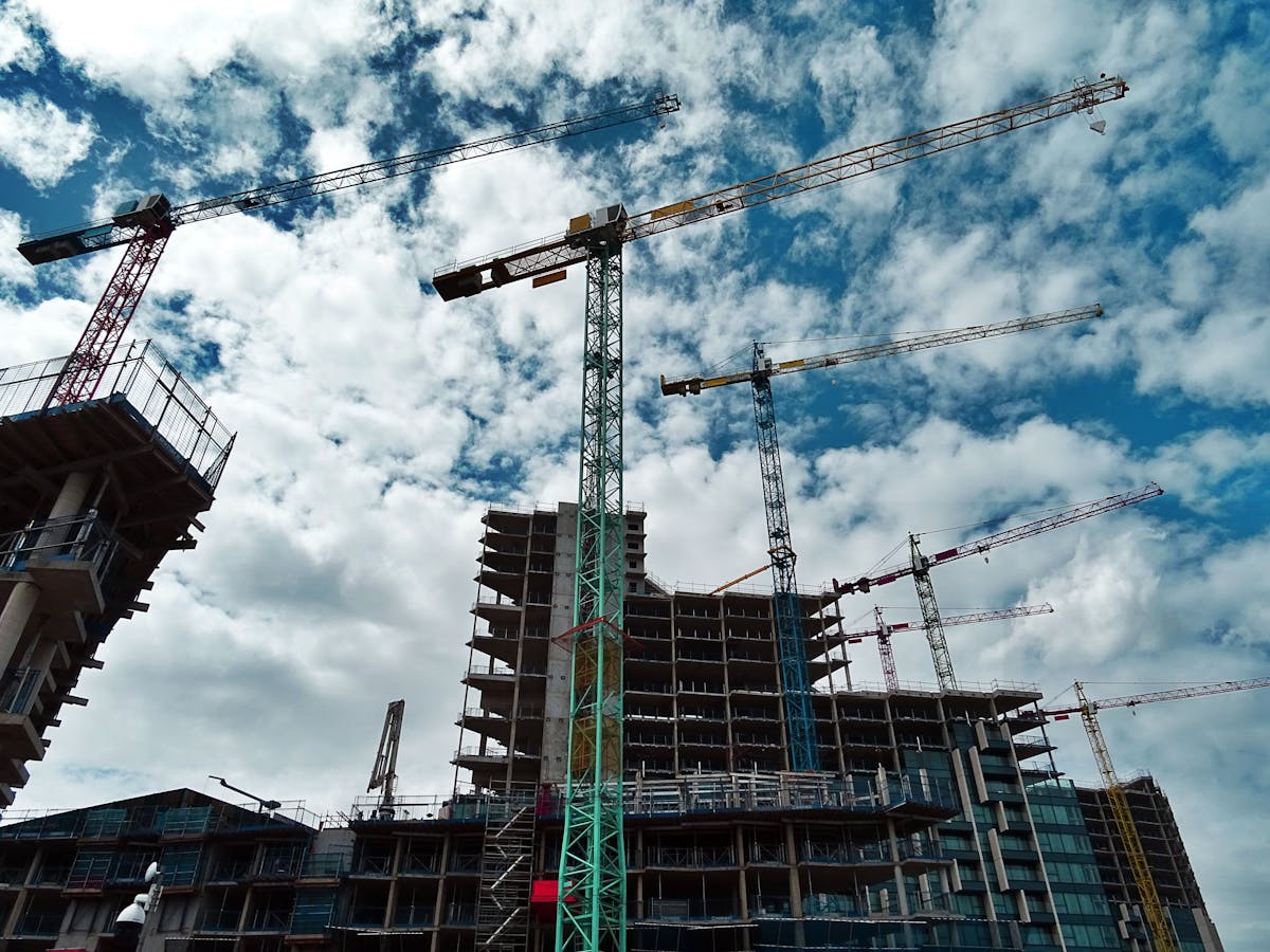 Skyscraper under construction with multiple cranes against a cloudy sky.