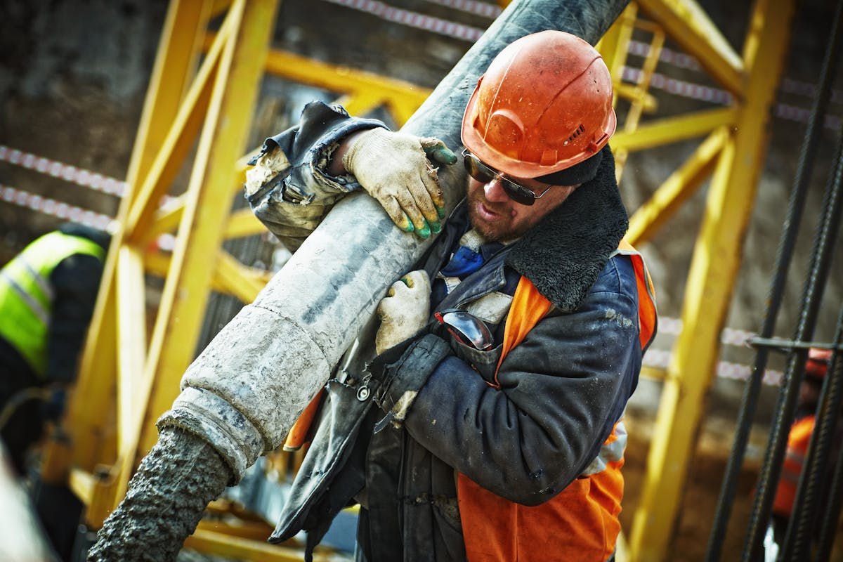 Construction worker in hard hat pouring concrete from a hose at a work site.