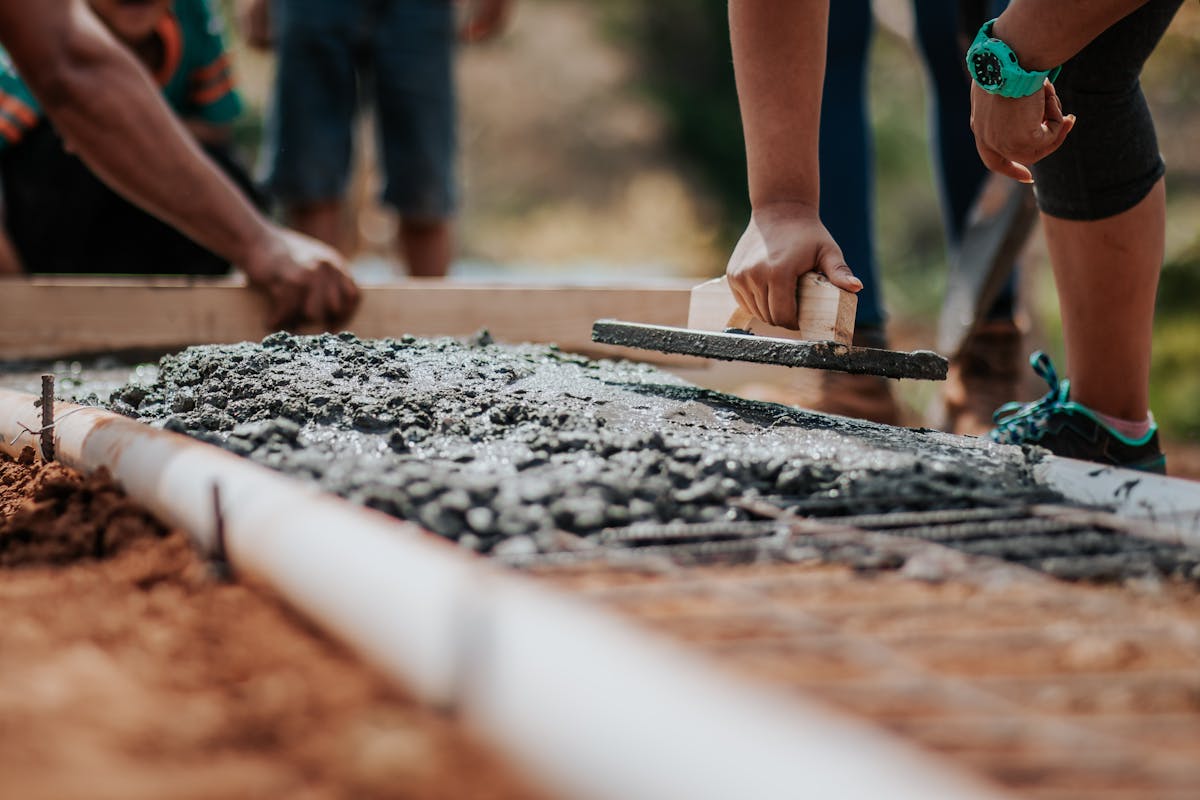 Workers spreading wet concrete with a trowel at a construction site.