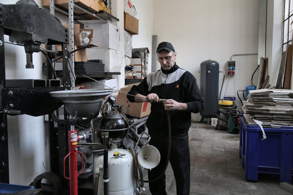 Man working with machinery in a workshop surrounded by tools, equipment, and stacked cardboard.