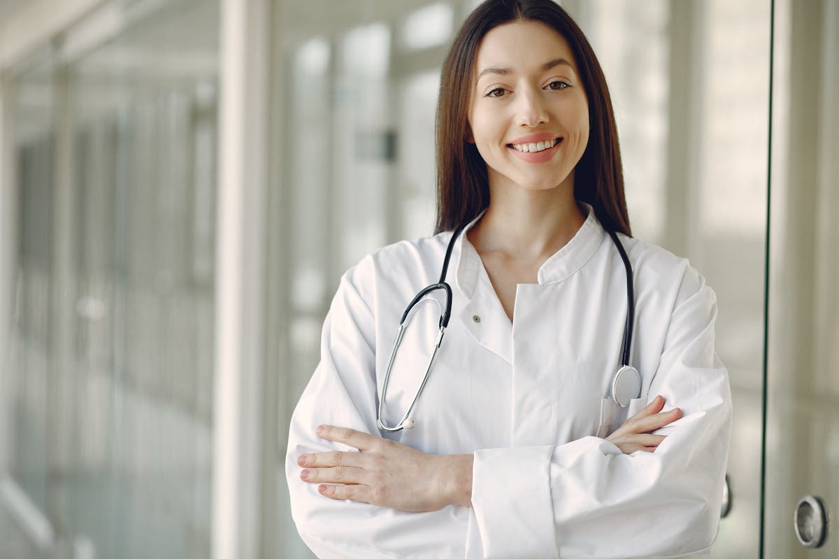 Smiling female doctor with stethoscope standing in hallway, arms crossed.