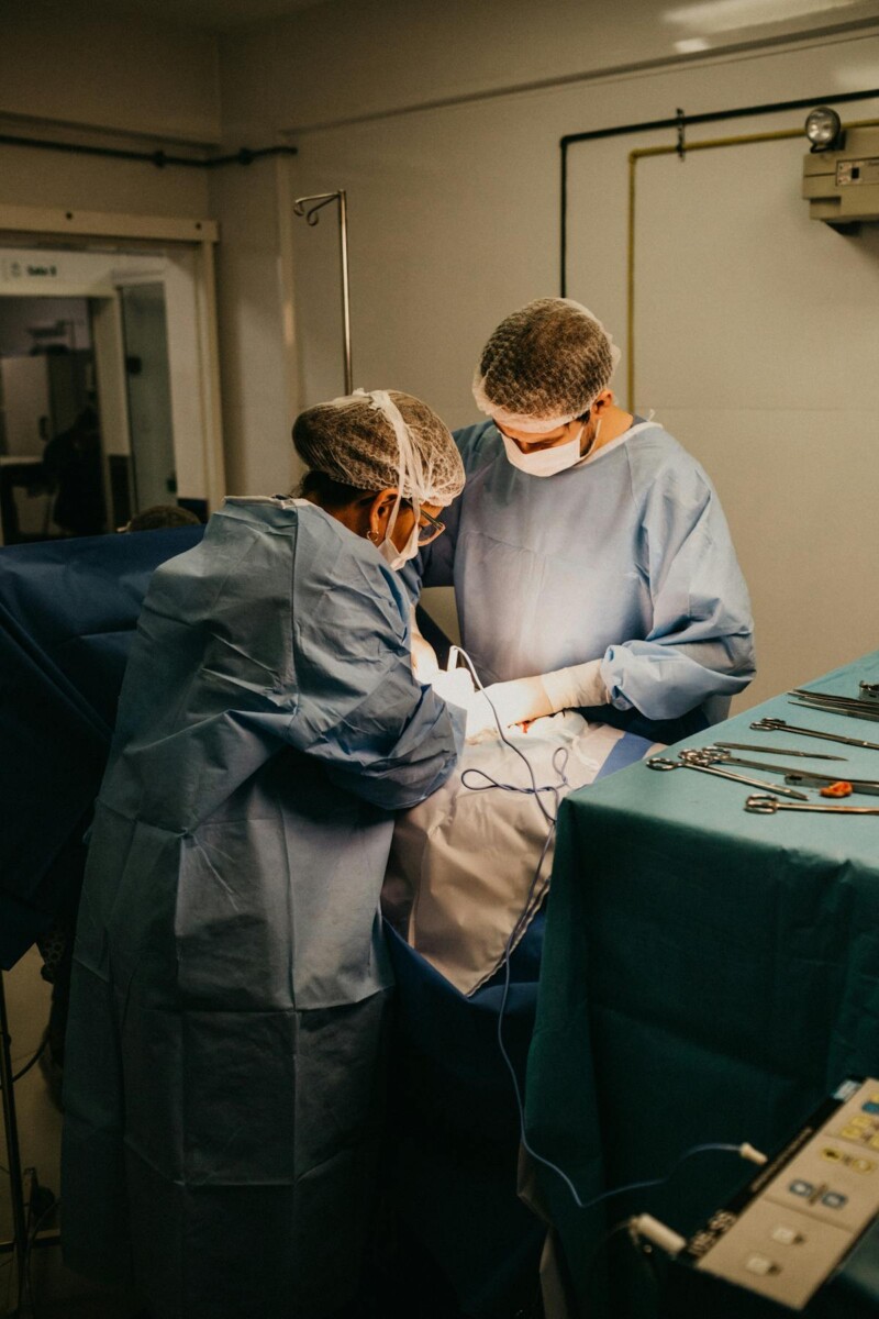 Two surgeons in blue scrubs performing surgery in an operating room, surrounded by medical instruments.