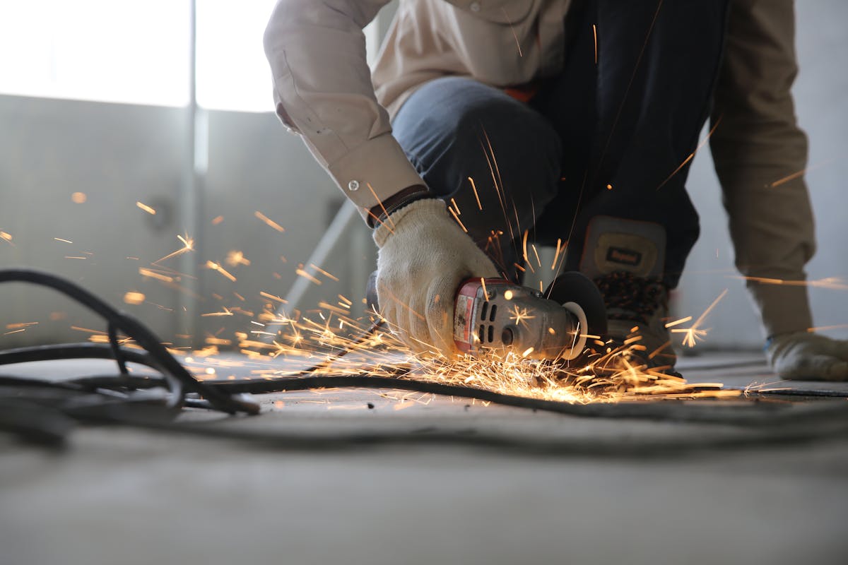 Worker grinding metal with an angle grinder, sparks flying.