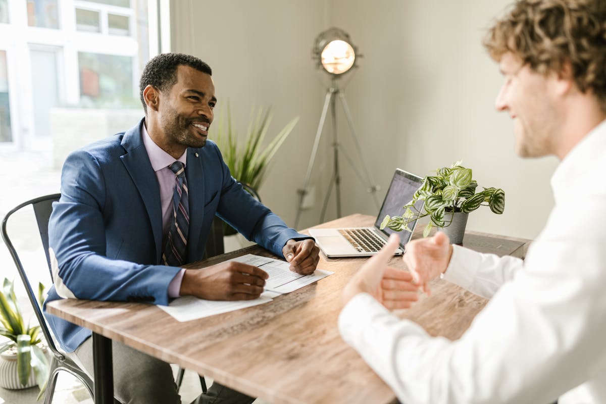 Two men having a lively discussion at a desk with a laptop and plant.
